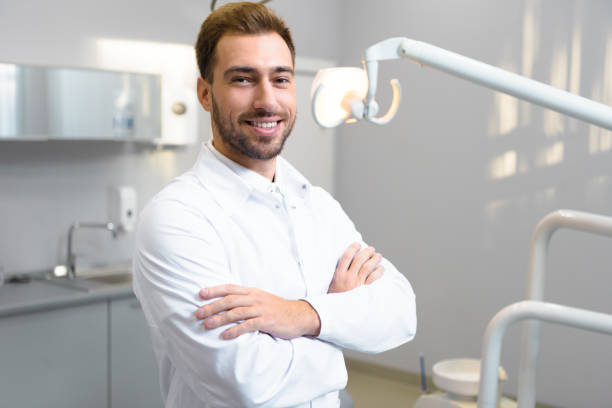 istock handsome young dentist with crossed arms looking at camera in office 1064214462