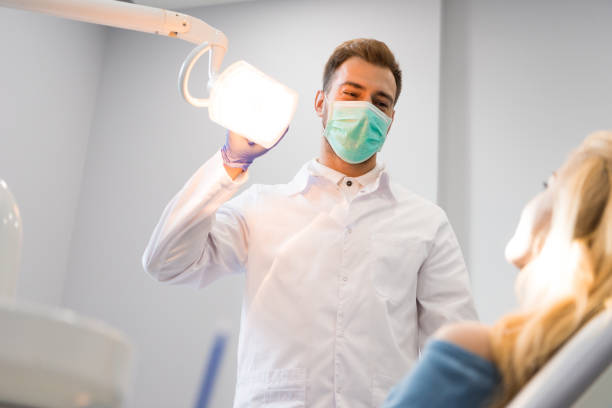 istock dentist in coat and mask standing over client with lamp 1064215800