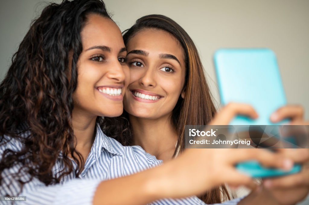 Two young women taking selfie on phone Two young Brazilian women photographing themselves on smart phone, posing, smiling, cheerful, social media Selfie Stock Photo