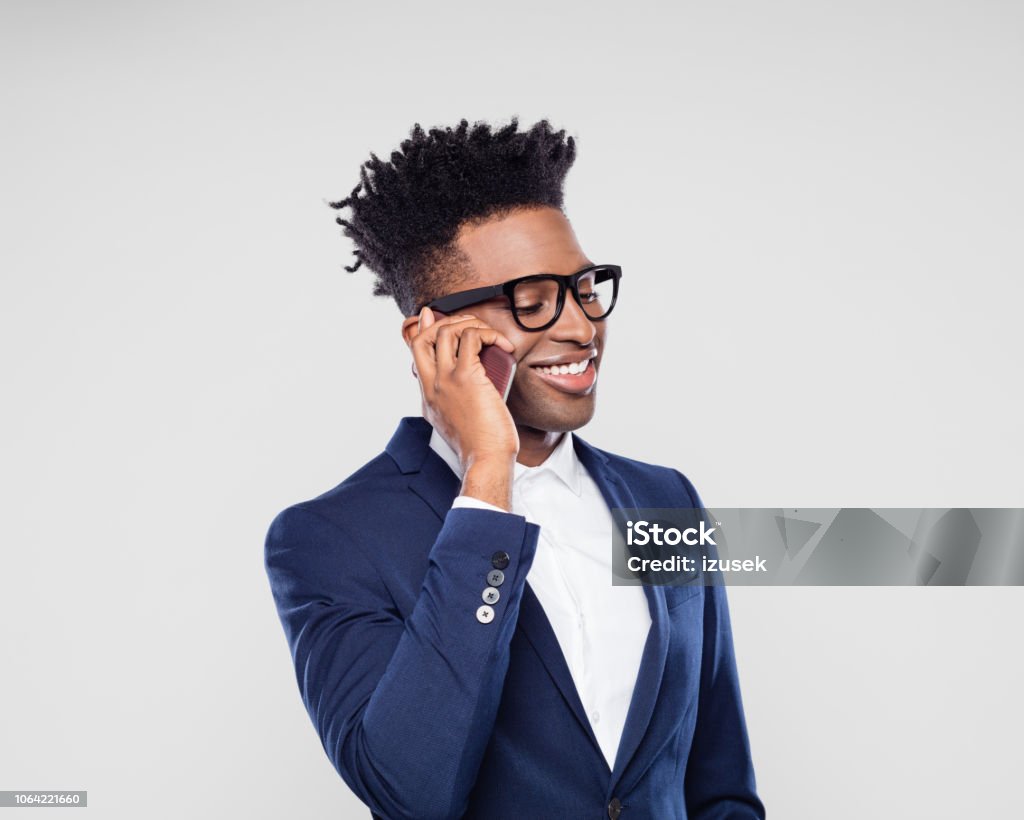Smiling businessman making a phone call Portrait of smiling african businessman talking on mobile phone against gray background. Happy young man in suit making a phone call. African Ethnicity Stock Photo