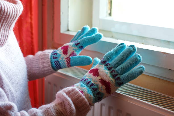 manos en guantes de lana en radiador - frío fotografías e imágenes de stock