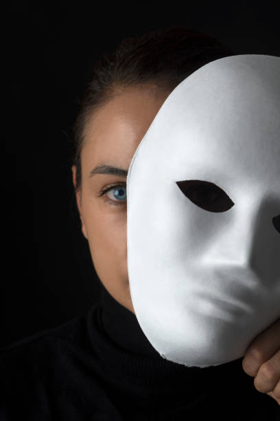 Hiding Female is hiding her face behind a white mask on black background. mask disguise stock pictures, royalty-free photos & images