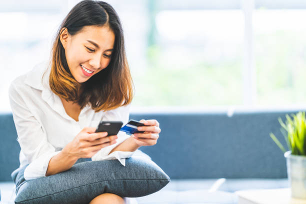 jeune belle femme asiatique à l’aide de smartphone et carte de crédit pour des achats en ligne à la maison avec l’espace de la copie. la technologie e-paiement, lifestyle accro du shopping ou téléphone mobile application financière concept - teenager retail shopping consumerism photos et images de collection