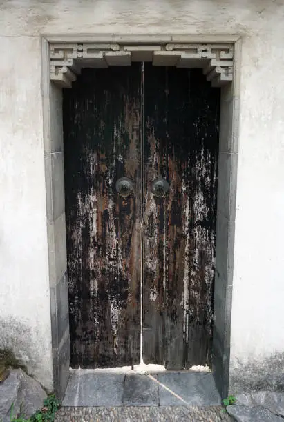 A distressed set of wooden doors set in a thick, concrete garden wall.