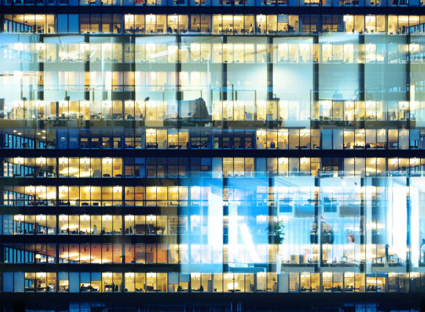istock Workers working late. Business finance building. Office windows by night. 1064261668