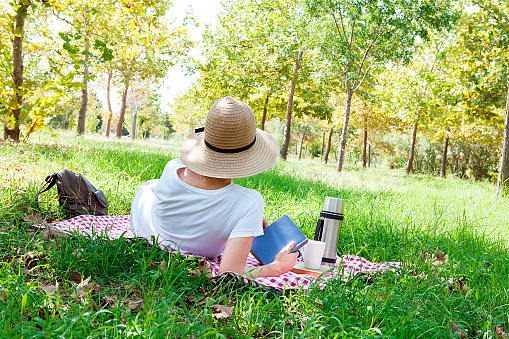 Young woman with book in hands is having a picnic in the countryside. Happy, cozy day, outdoors. Woman in park.