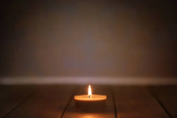 One tea light on a wooden table in front of a old wallpaper