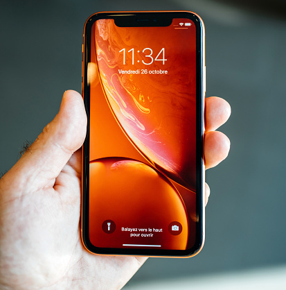 STRASBOURG, FRANCE - OCT 26, 2018: Happy owner POV holding new red iPhone XR smartphone admiring red wallpaper home lock screen - square image
