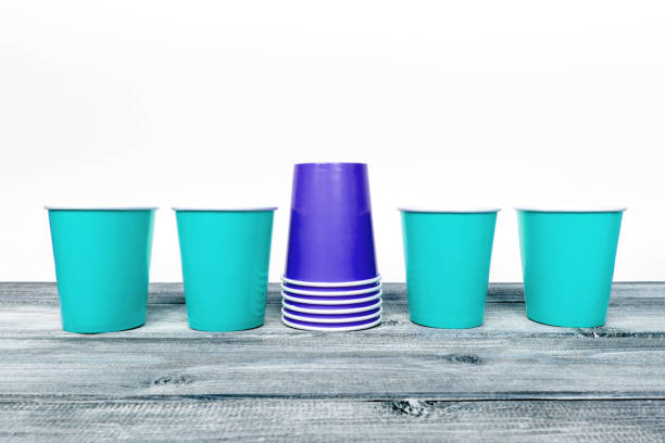 quattro vuote azzurre e una pila di blu rovesciato tovano i tazze di carta usa e getta su scrivania di legno e sfondo bianco - disposable cup cup stack blue foto e immagini stock