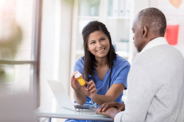 Female doctor explains new prescription drug to patient A smiling female doctor sits at a desk across from an unrecognizable male patient.  She wears scrubs as she points to a prescription bottle and gives instructions. pill bottle photos stock pictures, royalty-free photos & images
