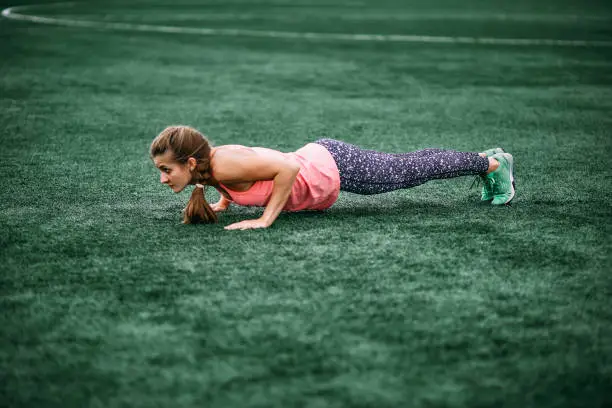 A beautiful muscular girl in tights and a vest makes a warm-up at the stadium. gym, fitness, healthy lifestyle