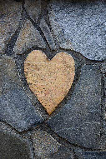 Close-up photo of a Heart Shaped Decorative Flagstone, pave stone or a stepping stone on a gray wall background. Romantic decoration, wall design.