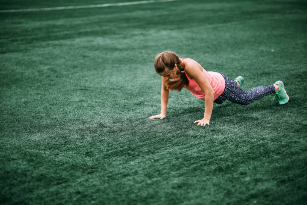 A beautiful muscular girl in leggings and a vest makes a burpee at the stadium. gym, fitness, healthy lifestyle stock photo