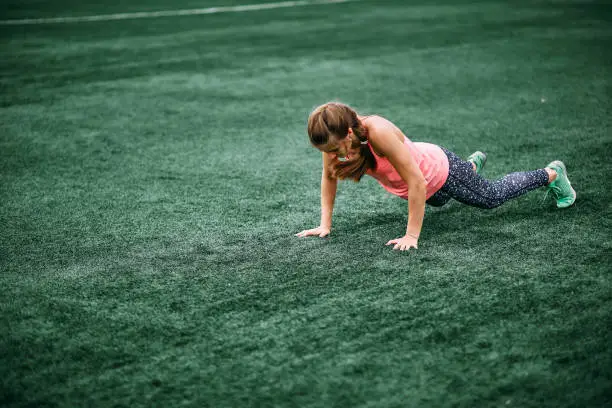 A beautiful muscular girl in leggings and a vest makes a burpee at the stadium. gym, fitness, healthy lifestyle