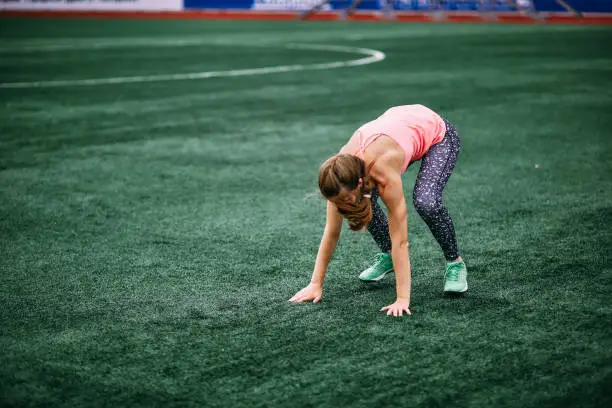 A beautiful muscular girl in leggings and a vest makes a burpee at the stadium. gym, fitness, healthy lifestyle