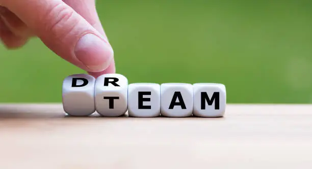 Hand is turning a dice and changes the word "dream" to "team"