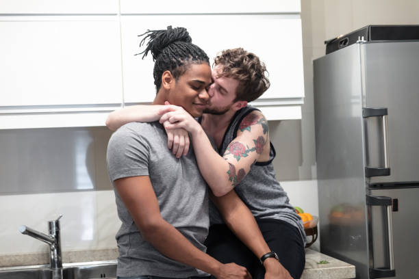 amor de hombre gay besando a su compañero abrazado a él mientras estaba sentado en el mostrador de la cocina - gay man homosexual men kissing fotografías e imágenes de stock