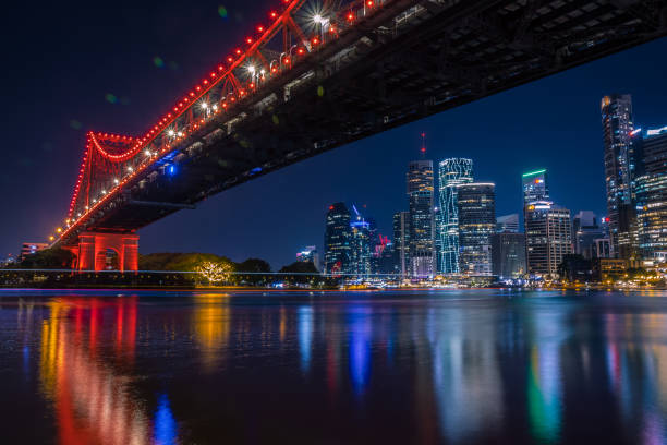 Modern bridge construction crossing city river and reflecting in water with bright lights, Brisbane