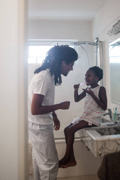 istock Beautiful daughter washing her teeth on the bathroom while rasta daddy talks and smiles at her 1064385344