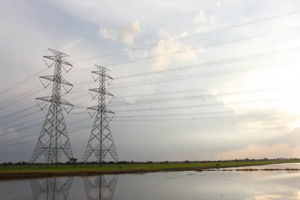 The sun is shining,Hight power transmission tower are located on a green field.Many wires are tied a cross The water to see the full field.