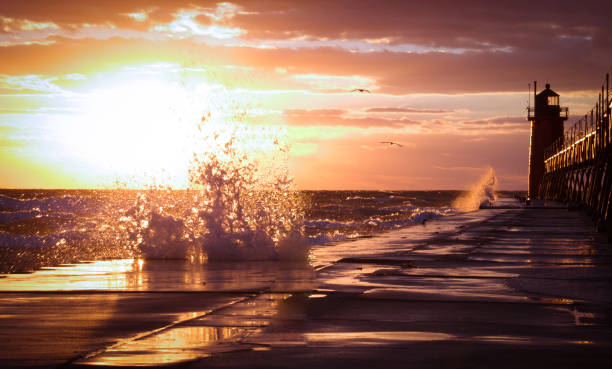 crashing waves on lighthouse pier. vibrant weather sunset. - lake michigan sun sunlight nature imagens e fotografias de stock