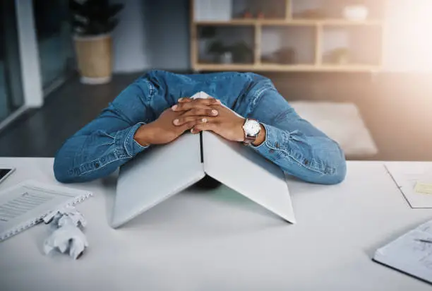 Shot of a businessman lying down on a desk with a laptop over his head in an office