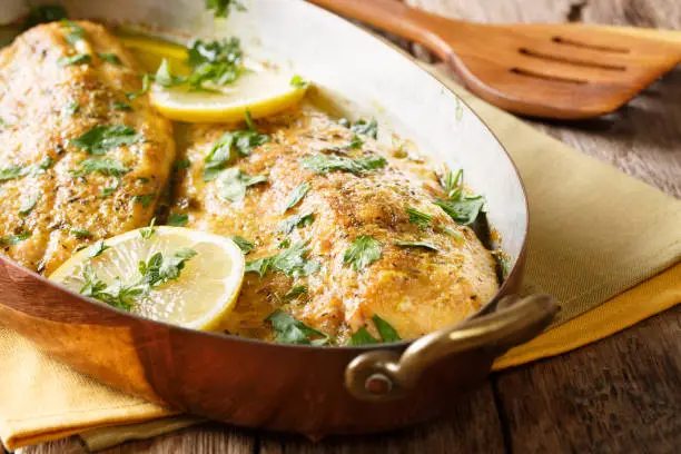 Photo of Delicious fish: baked trout fillets with garlic buttery herb sauce, lemon and parsley close-up in a copper pan. horizontal