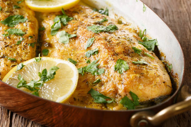Delicious food: trout fish with garlic lemon butter sauce, parsley close-up in a copper frying pan. horizontal stock photo