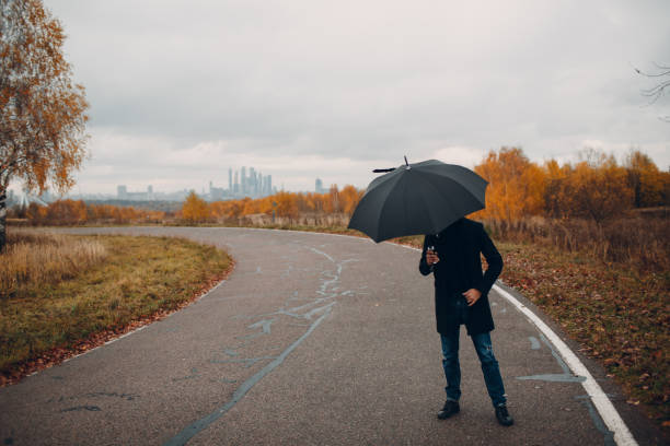 istock Young man in black coat walking in the rain with umbrella 1064458924