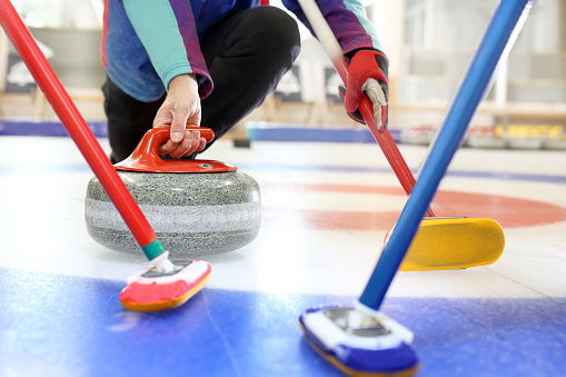 Curling games. The player is brushing the ice by directing the stone to the house