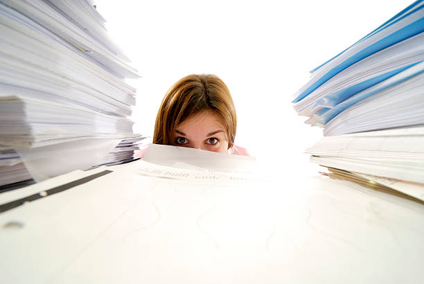 istock young woman looking from behind a stack of papers 106447903