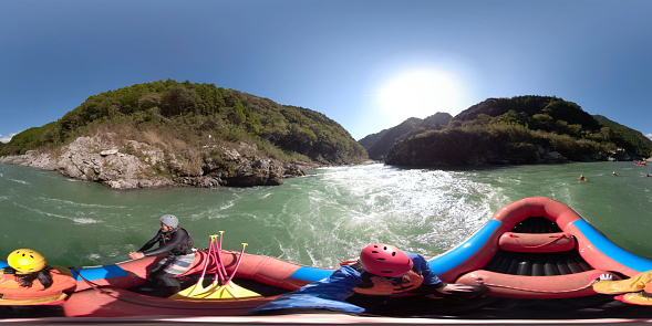 360 degree VR image of a small group of men and women white water river rafting in a forested valley in Japan.