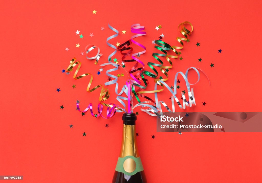 Champagne bottle with colorful streamers top view Champagne bottle with colorful party streamers on red background Champagne Stock Photo