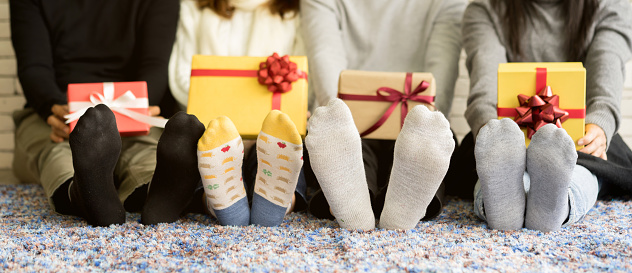 close up group of diverse friends feet with socks holding gift boxes and sitting on carpet mat in living room at home for christmas and happy new year party concept