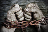Powerful male hands clenched into fists and chained with old rusty thick chain