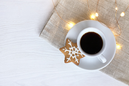cup of black coffee with ginger cookies in the shape of a star with festive garland on the table top view