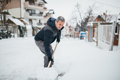 Man with snow shovel cleans sidewalk in winter