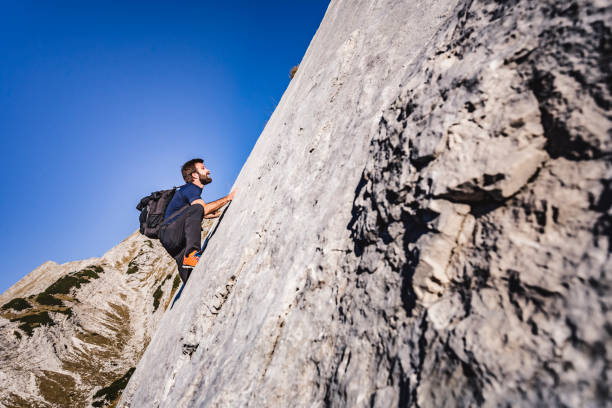 Climber in a steep wall looking for the way up Side-view shot of an athlete climbing a steep reef in the Julian Alps. steep photos stock pictures, royalty-free photos & images