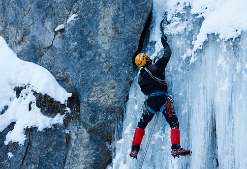 Frozen waterfall climbing during winter season with professional safety first equipment.