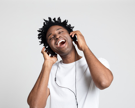 Portrait of young afro american man enjoying listening to music on headphones against gray background.