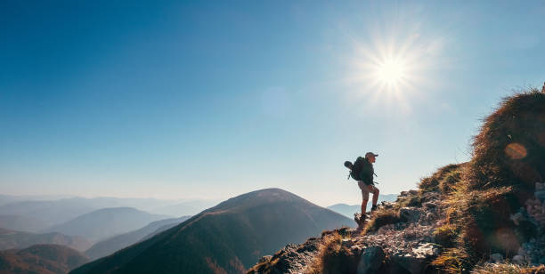istock Boy backpacker traveler walk up on mountain top in contrast sun light 1064532732
