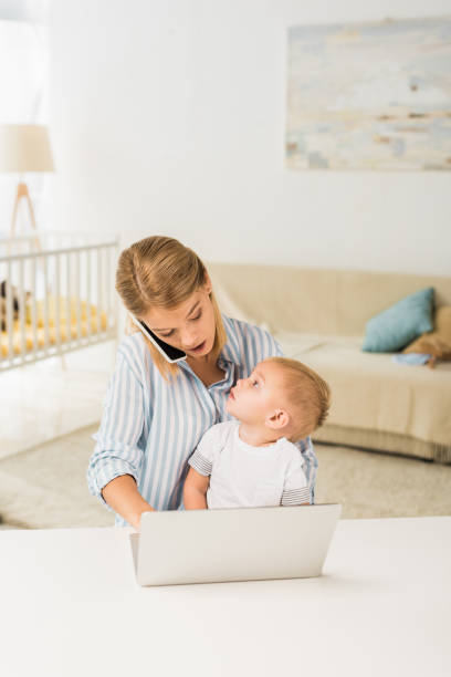 istock mother sitting at desk with cute toddler while talking on smartphone and using laptop 1064547694
