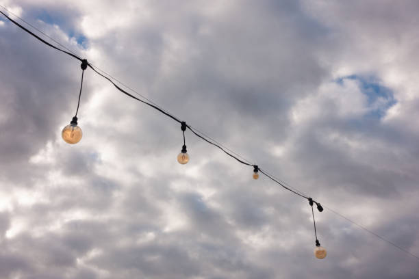 String of orange light bulb decoration against cloudy sky.