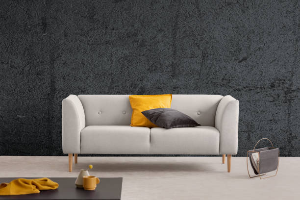 istock Yellow and black pillow on grey sofa in living room interior with textured wall and table. Real photo 1064553036