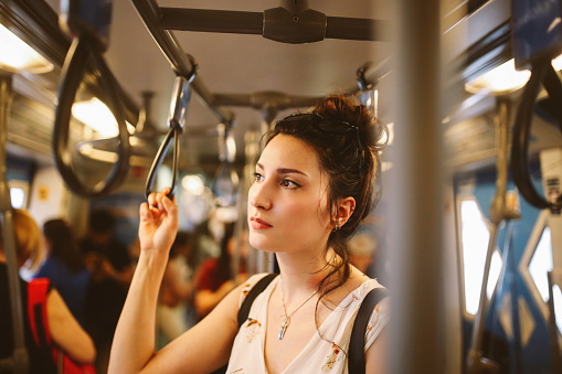 Young tourist woman moving around Bangkok, using public transport. She is tired, standing in the subway wagon, waiting for her station.