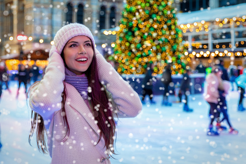 Beautiful, young woman in winter knit clothes on a Christmas market enjoys the falling snow