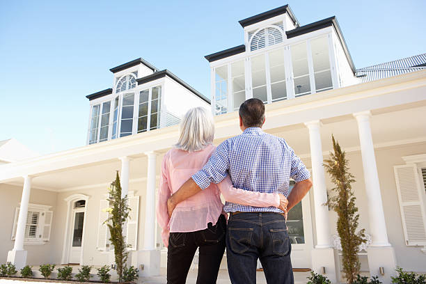 Senior couple embracing outside white colored house Senior Couple Standing Outside Dream Home show home stock pictures, royalty-free photos & images