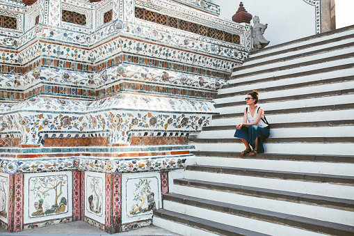 Young tourist woman enjoying her day in the famous Wat Pho Buddhist temple in Bangkok, Thailand. She is walking on a nice, sunny day, contemplating, enjoying the rich history of the famous place.