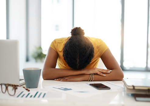 Shot of a young businesswoman with her head down on her office desk