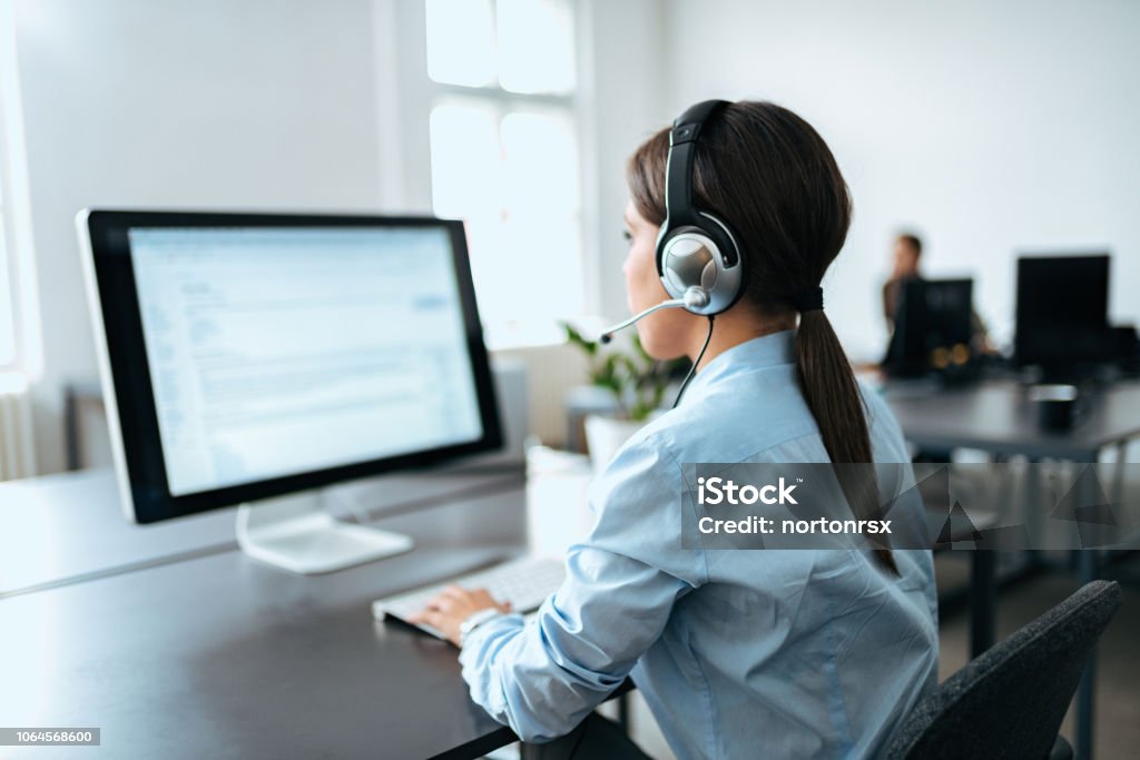 Female customer service representative with headset working on computer. Rear view. Customer Service Representative Stock Photo